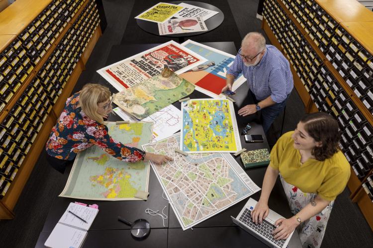 Three Library staff looking at collection items including maps and posters